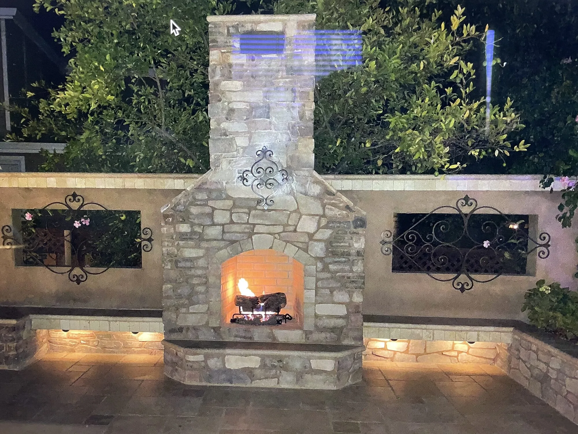 A lit stone fireplace centered between built-in benches on the evening gathering terrace.