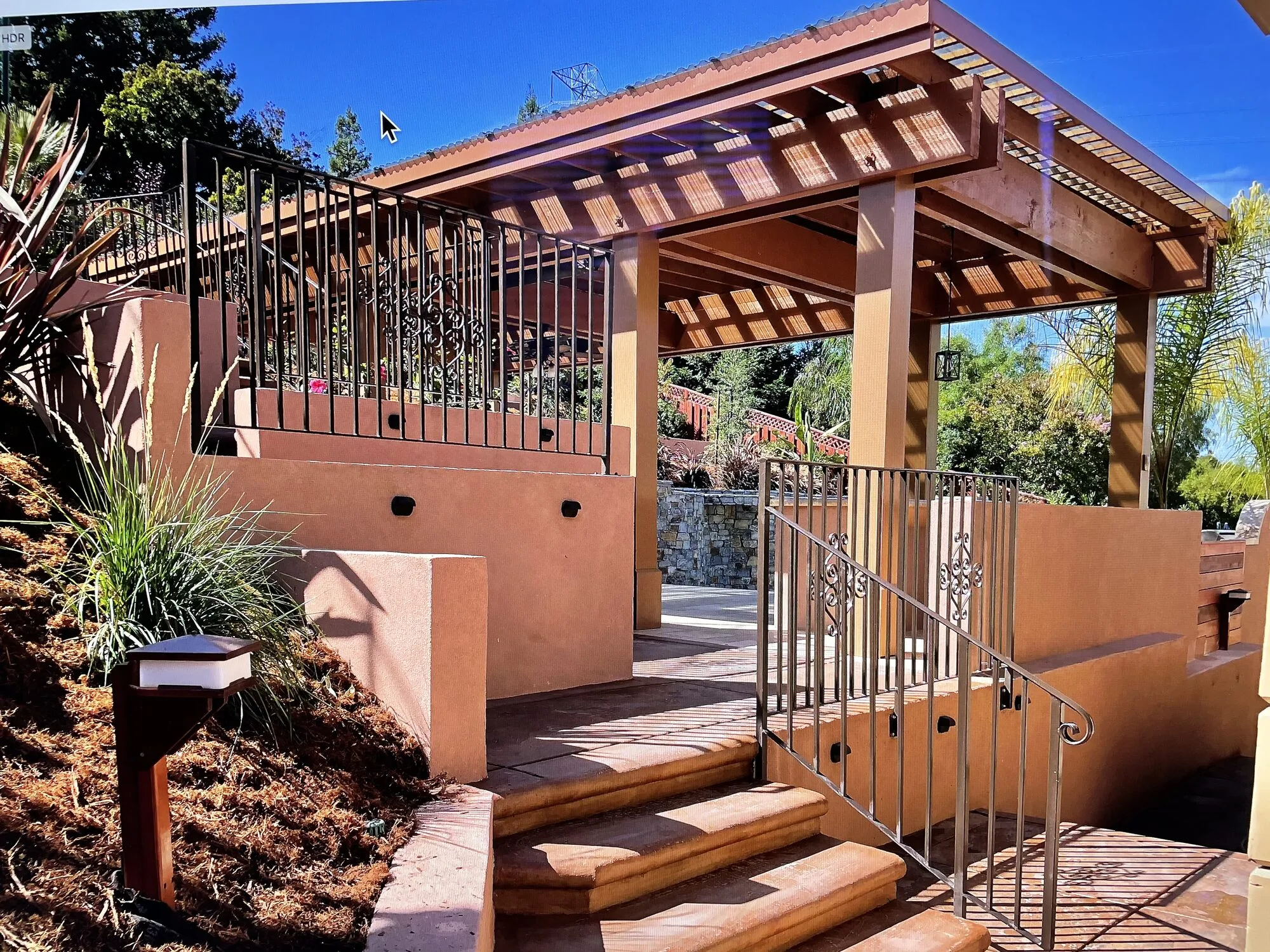 An open-sided lanai reached by garden steps and bordered by planted retaining walls.