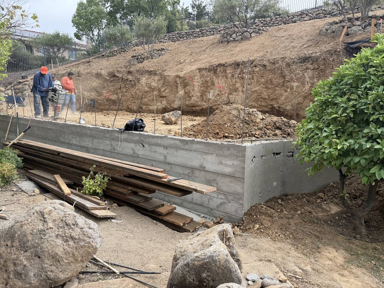 A concrete retaining wall taking shape along the excavated hillside.
