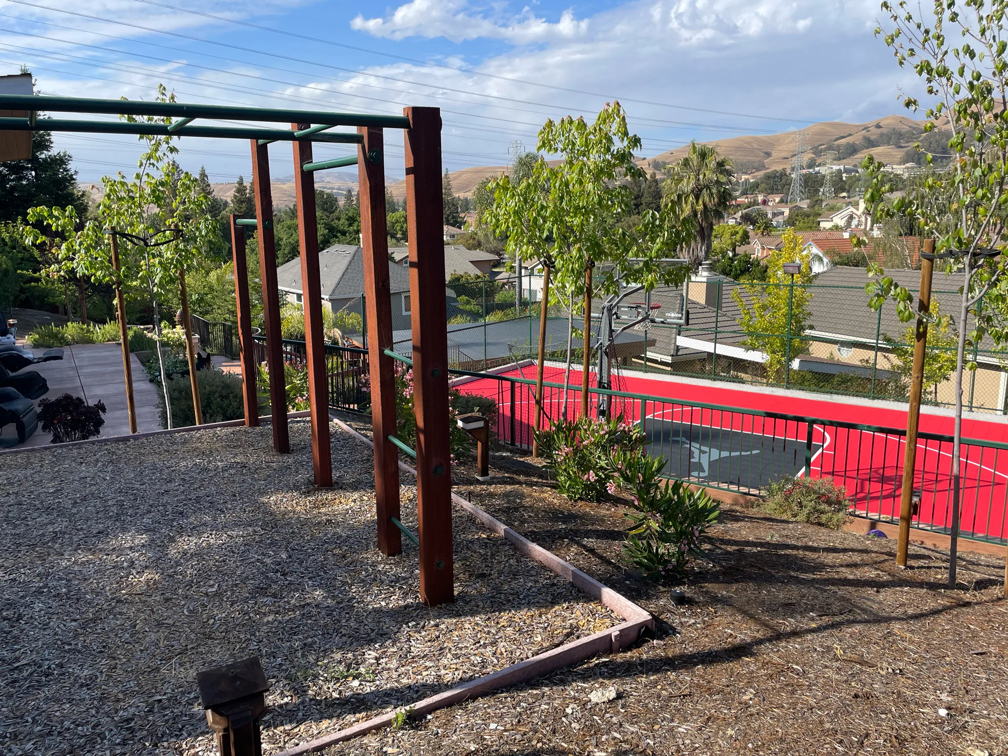 Exercise bars and young trees occupy the upper garden above the sport court, with the Fremont hills visible beyond.